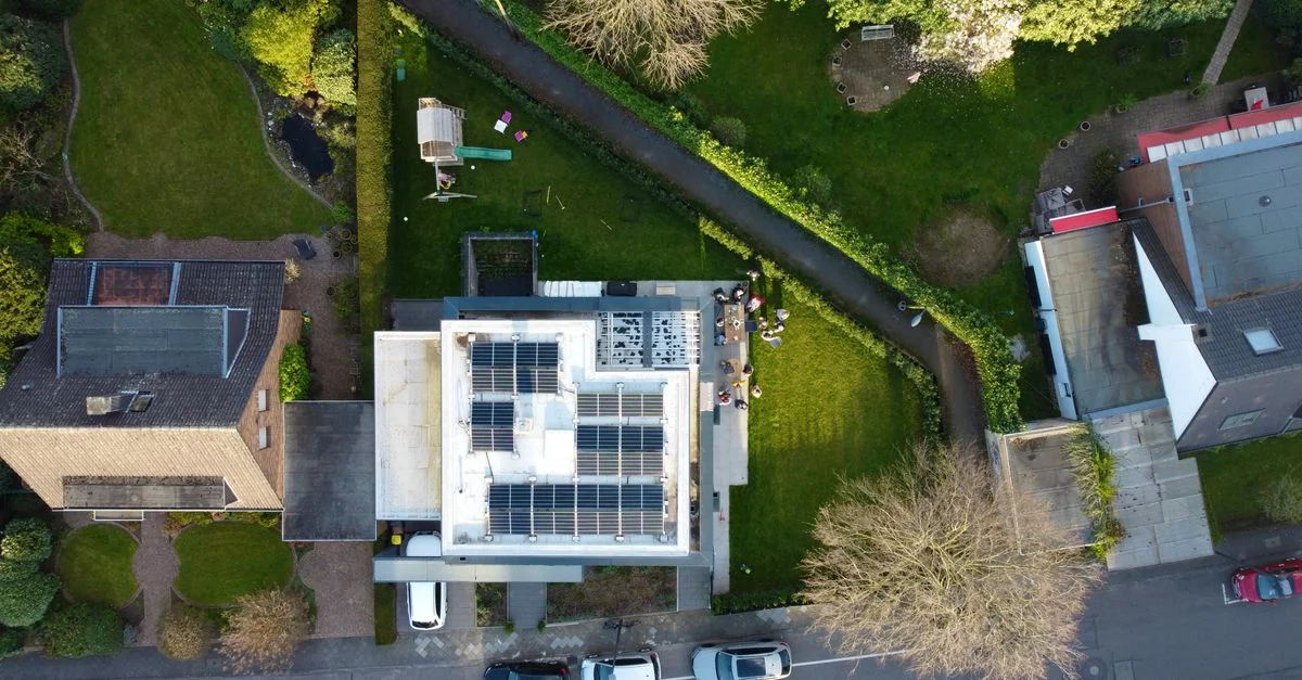Vue aérienne de maisons suburbaines avec des panneaux solaires sur les toits et des jardins verts.